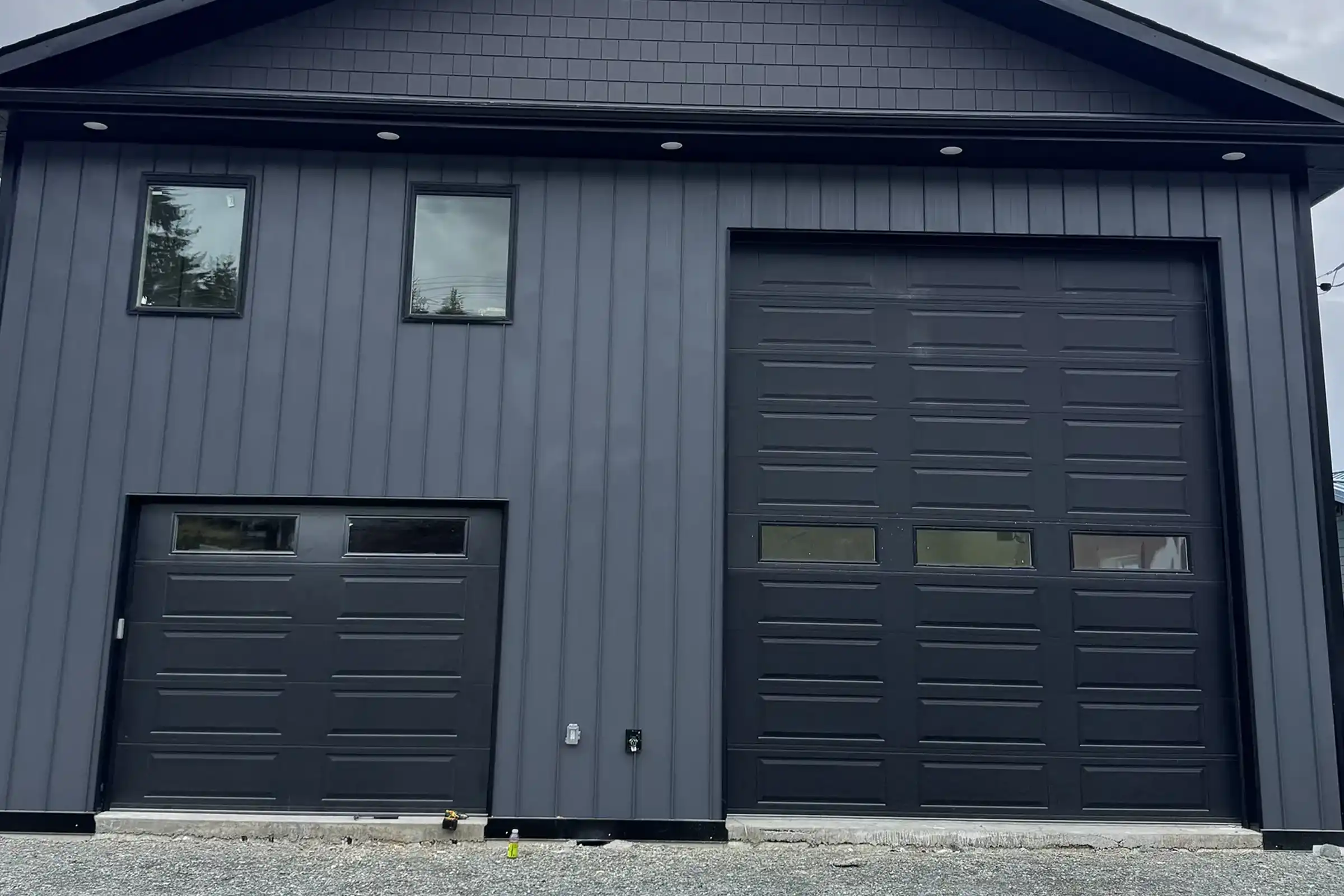 Two black garage doors with window lites on a dark gray board-and-batten shop