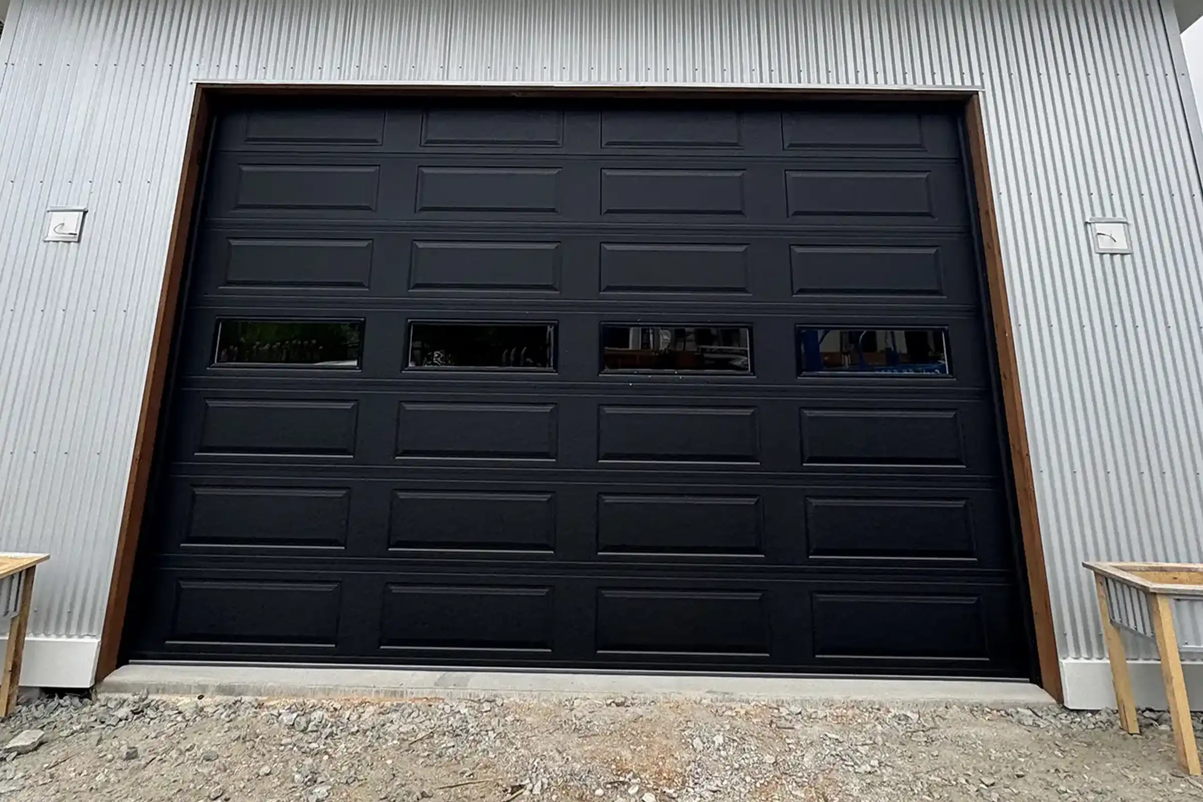 Black raised-panel garage door with a row of window lites on a metal-sided building